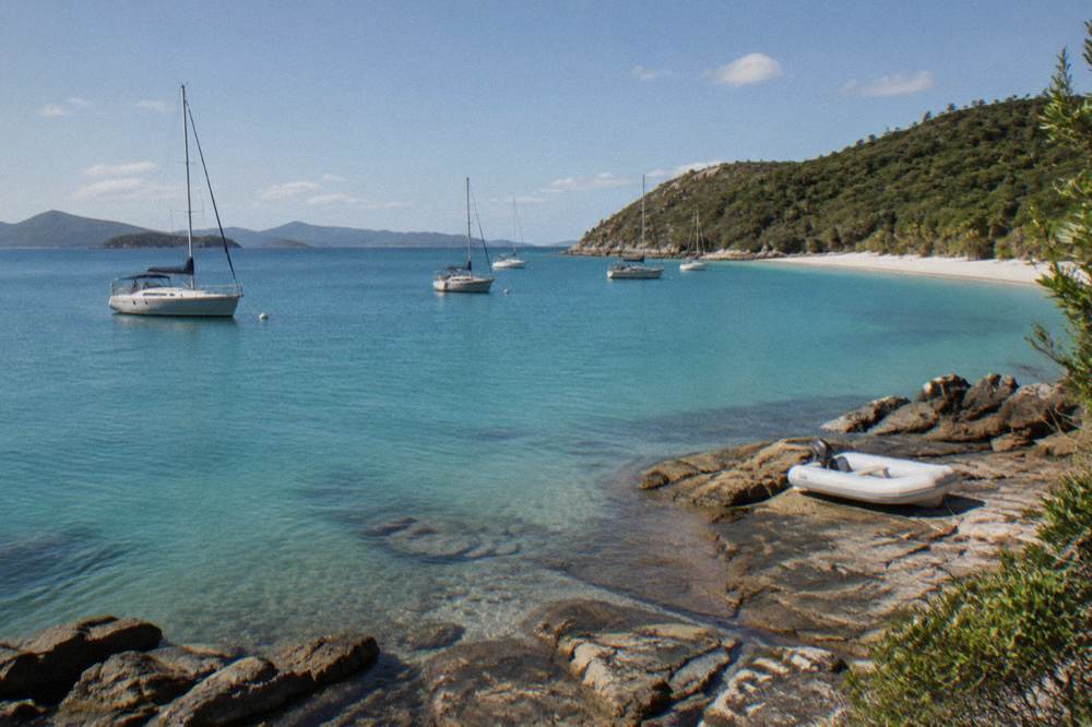 Sailing yachts moored in a calm bay fringed by white sand and headland scrub