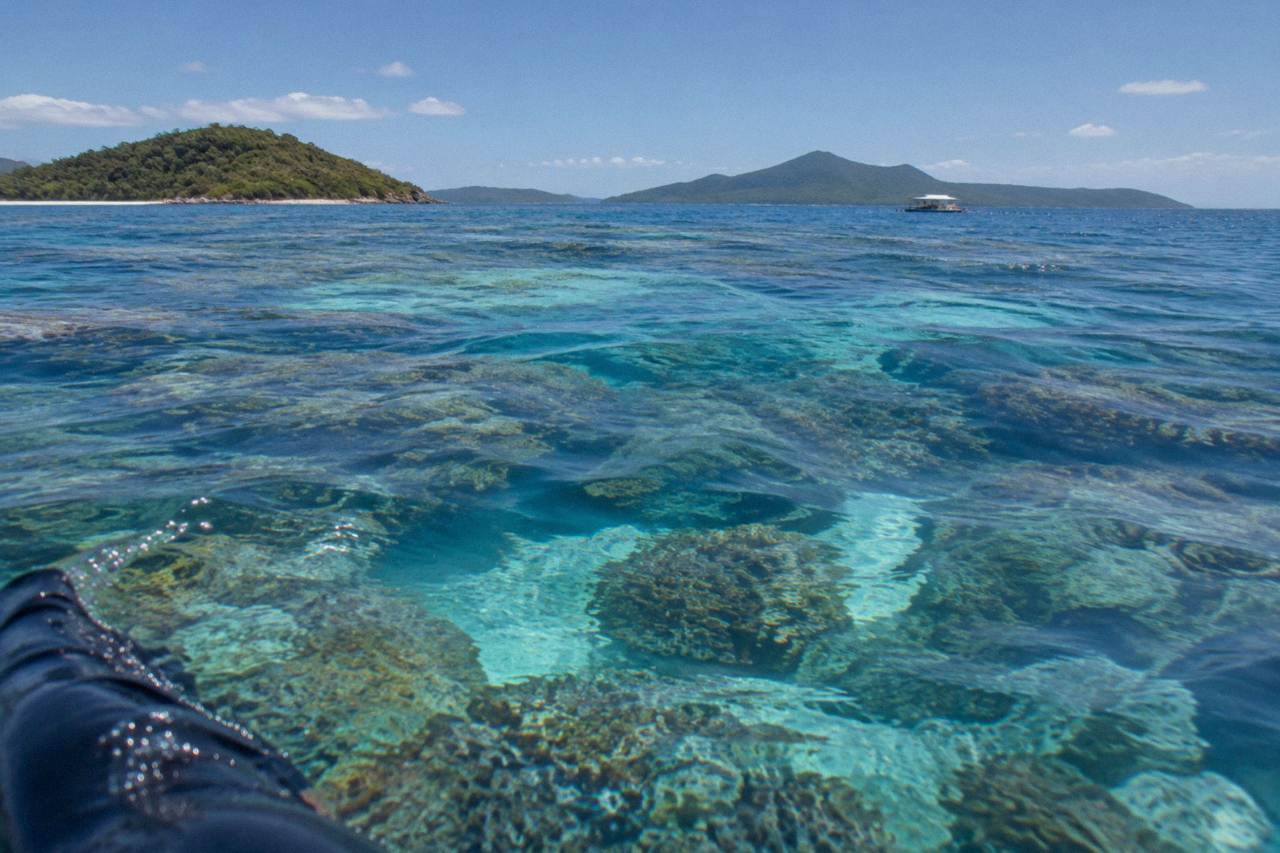 Clear turquoise water over a coral reef with shallow sand patches and distant green islands