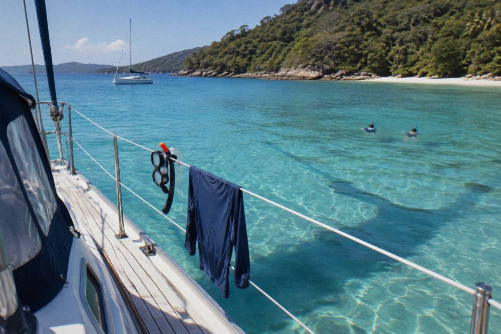 A sailing yacht moored in clear blue water beside a wooded island