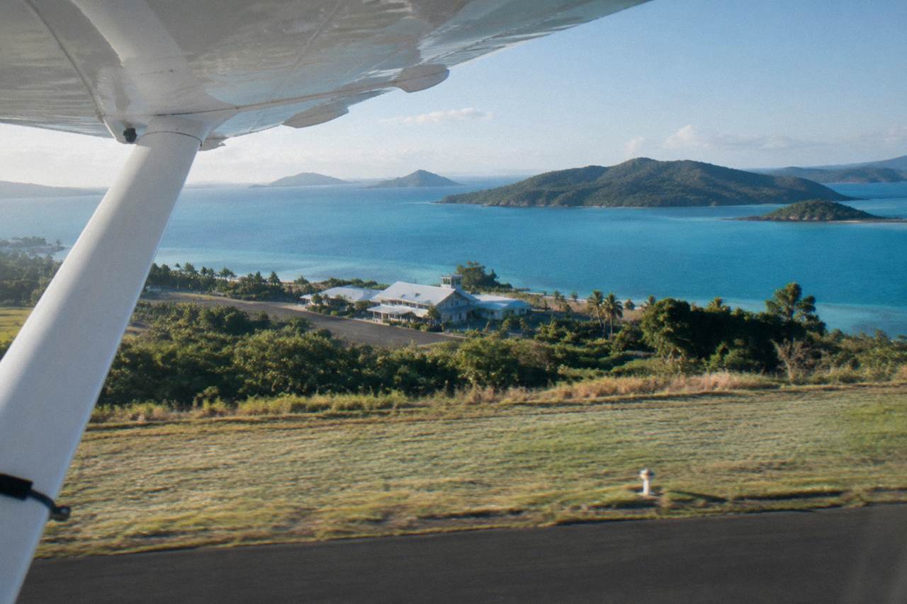 A light aircraft wing above turquoise reef water and green islands of the Whitsundays