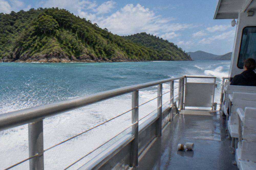 A passenger ferry cruising past densely forested tropical islands on calm turquoise water