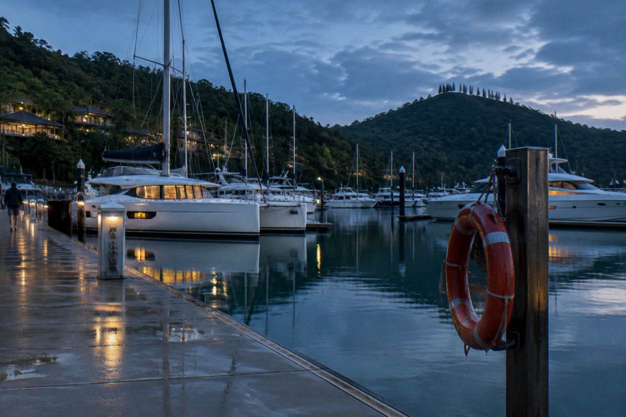 Yachts moored in a tropical island marina at dusk with calm water and forested hills behind
