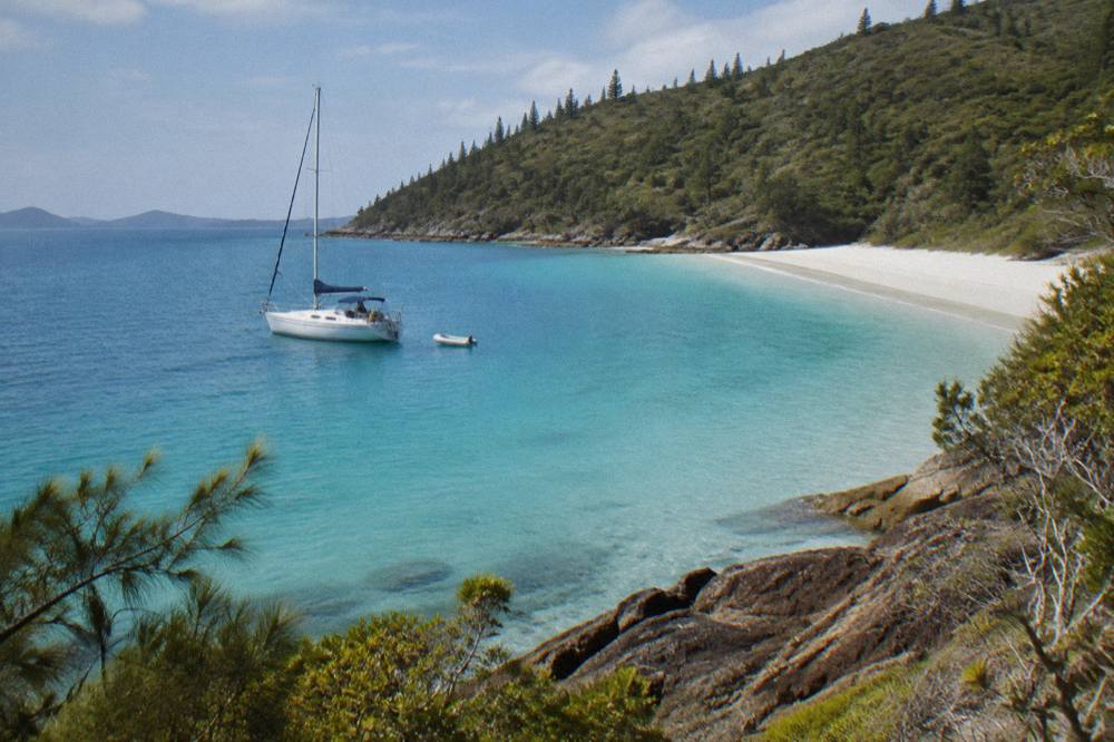 Yacht anchored off a white sand beach with turquoise shallows and green island hills