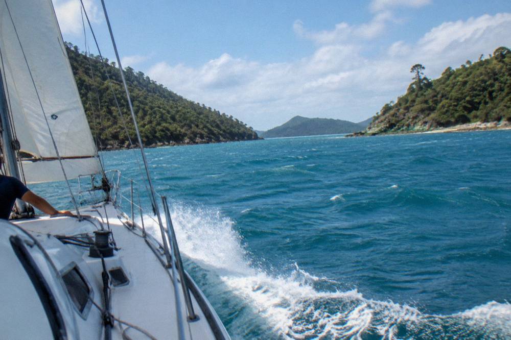 Sailing yacht heeling through blue water between green Whitsunday islands