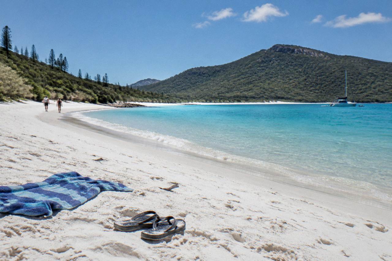 White sand beach curving into turquoise inlet water between forested hills