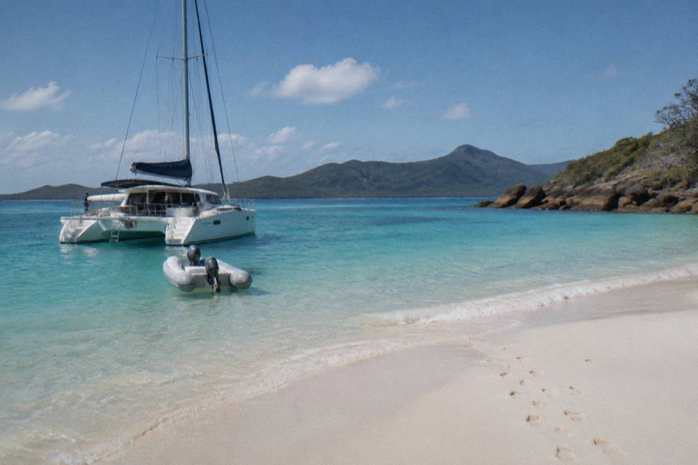 A sailing catamaran moored close to a white sand beach in clear turquoise water