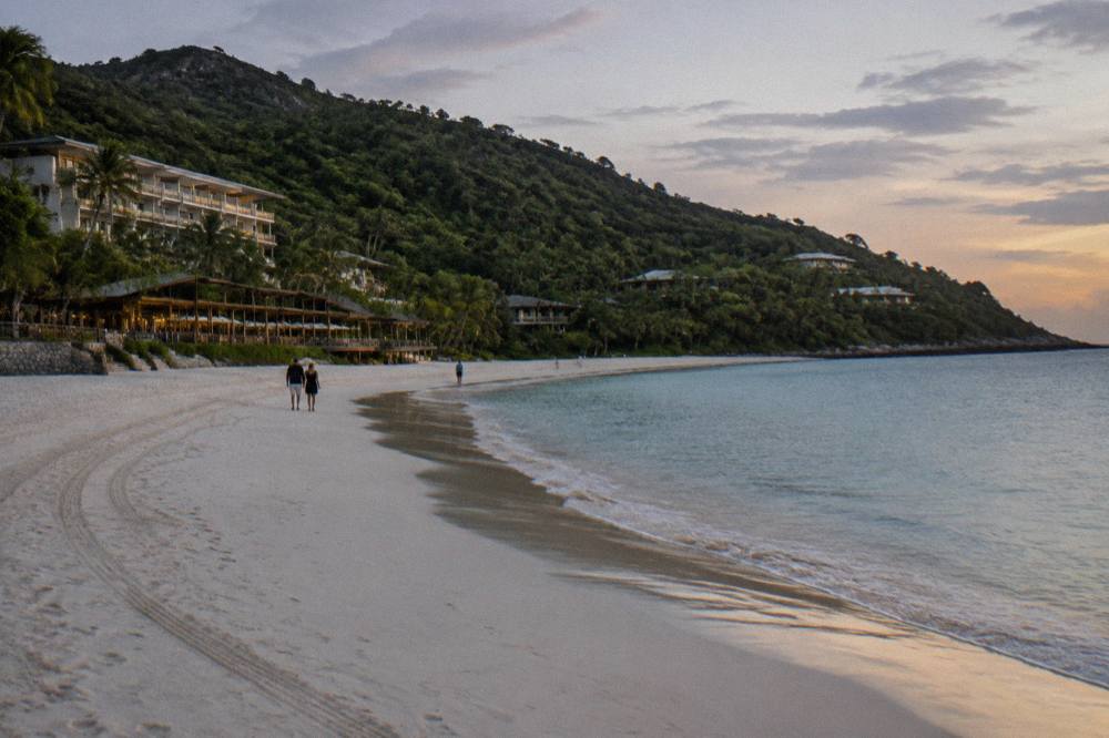 Aerial view of a white sand beach curving between dense green island hills and clear blue sea
