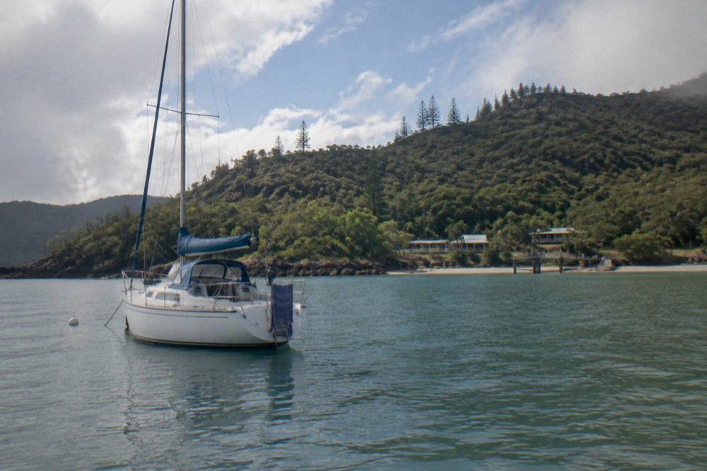 A sailing boat anchored near wooded islands under a clearing sky after rain