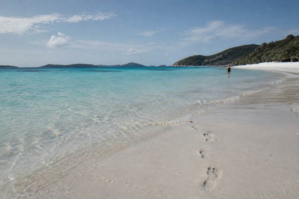 Calm turquoise shallows along a long white silica sand beach under a wide sky