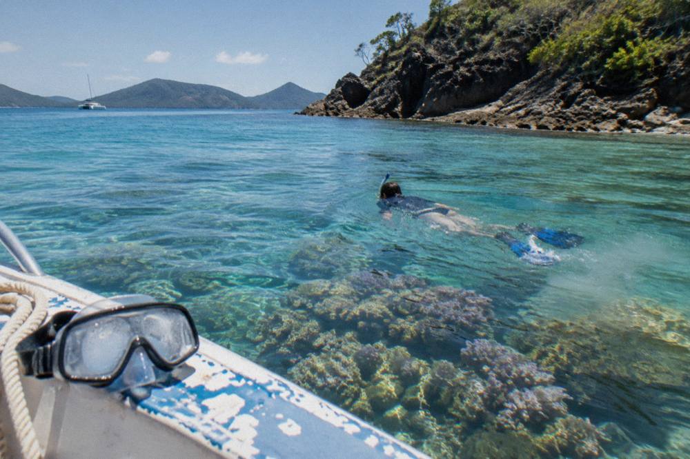 Snorkeller floating over coral beside a rocky island headland