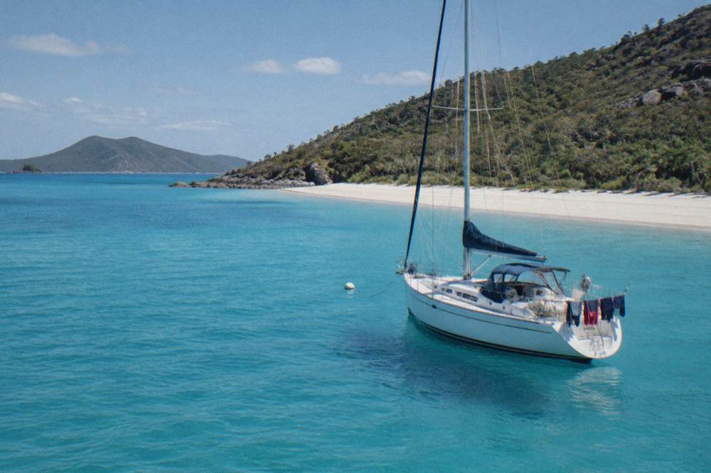 Anchored sailing yacht off a long white beach under a clear sky