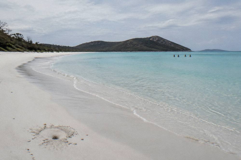 White silica sand curving into turquoise water at Whitehaven Beach under scattered clouds