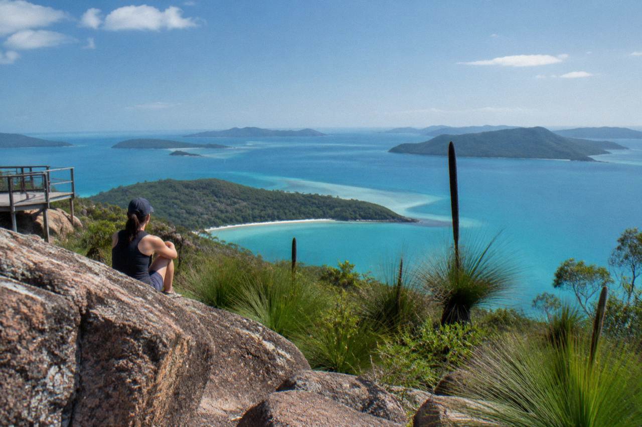 Calm turquoise water and green forested islands under a wide blue sky in the Whitsundays