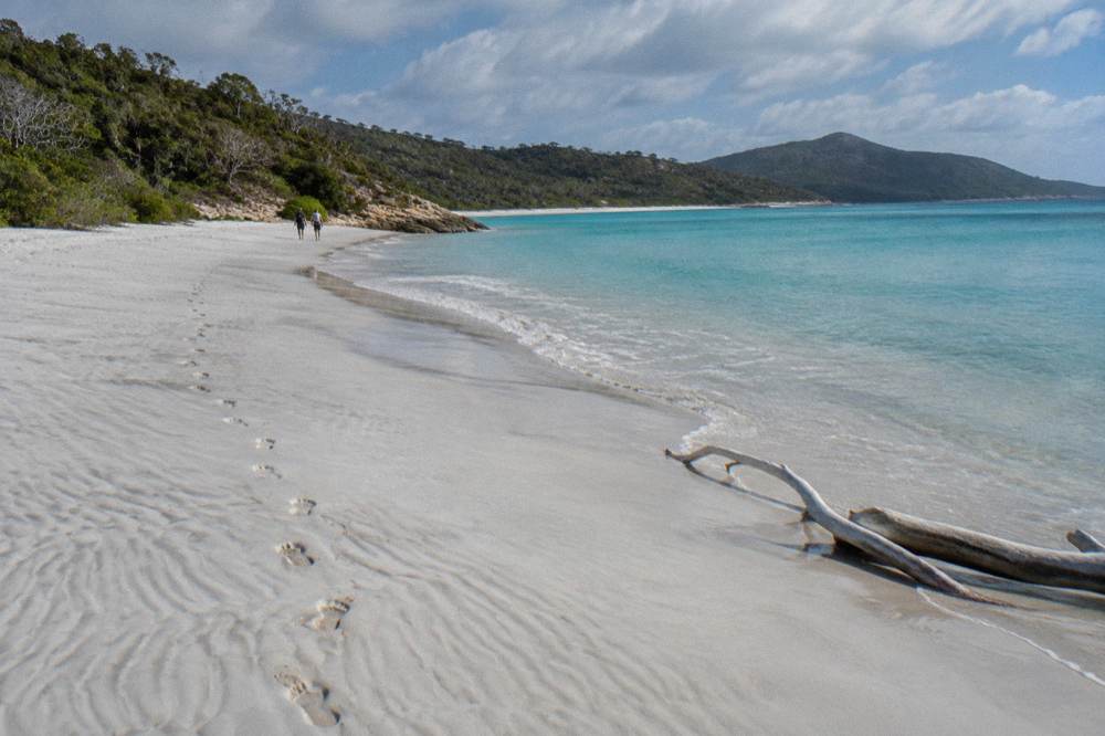 A wide stretch of white sand beach curving toward a turquoise inlet