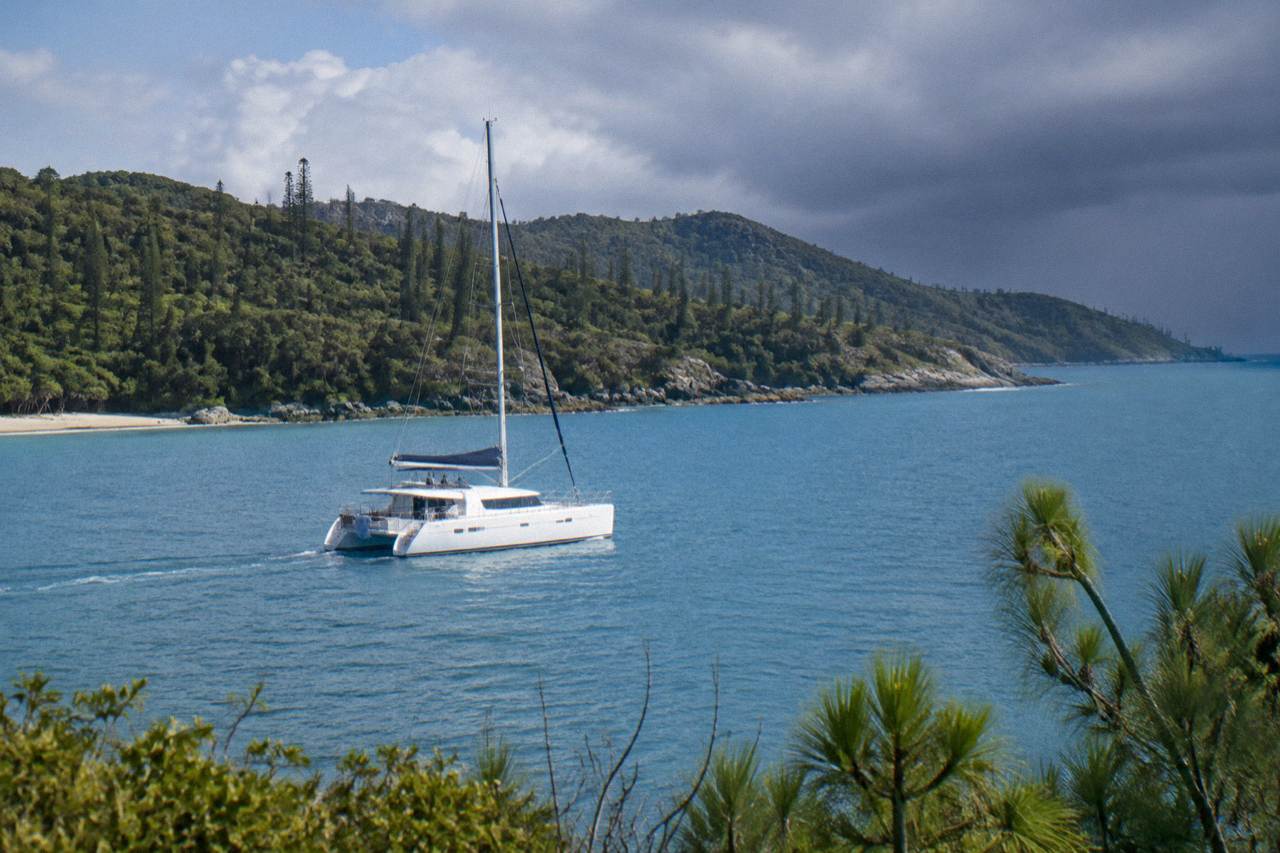 A large white catamaran cruising past green Whitsunday islands on calm blue water