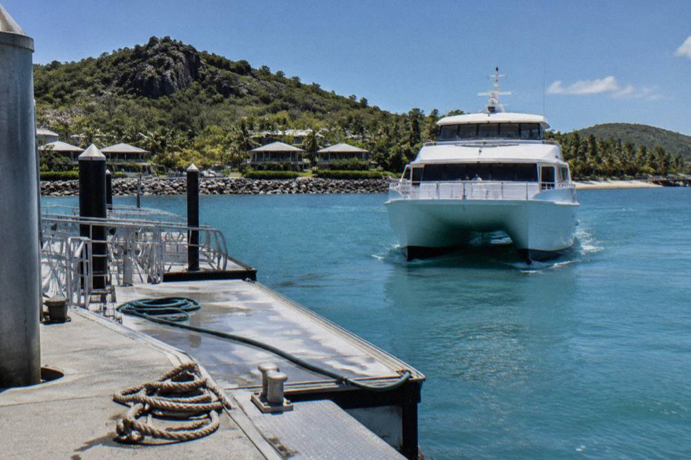 A passenger ferry approaching a tropical island jetty in calm blue water