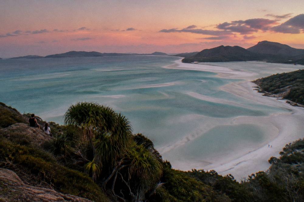 A long white silica sand beach meeting turquoise inlet water seen from a headland