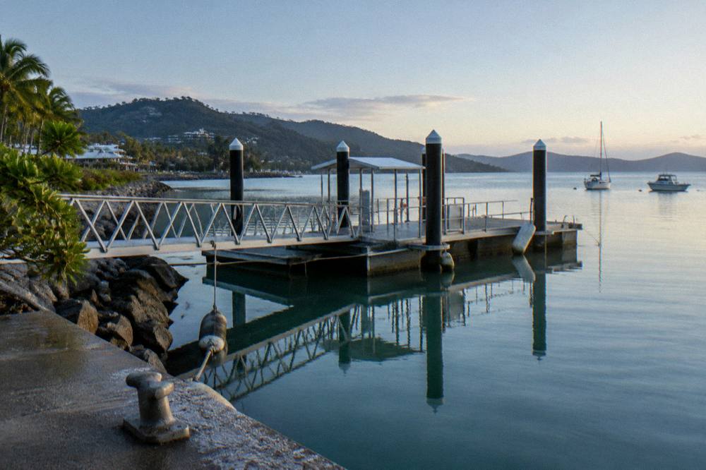 A ferry terminal jetty with calm morning water and anchored boats
