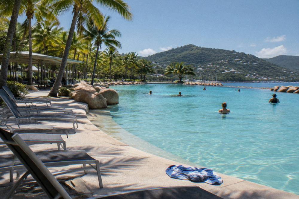 Large swimming lagoon with palm trees and deck chairs beside a sheltered pool edge