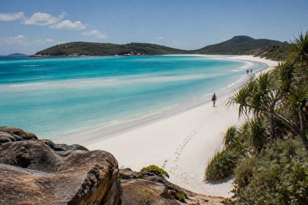 Long curve of white sand beach meeting turquoise shallow water between green headlands