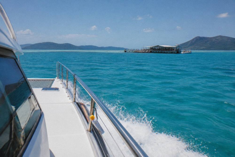 A fast catamaran cruising across open turquoise water toward a reef pontoon