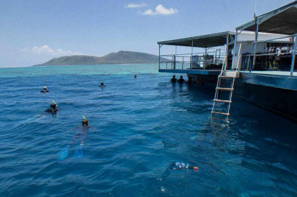 A reef pontoon moored in open blue water with snorkellers in the water beside it