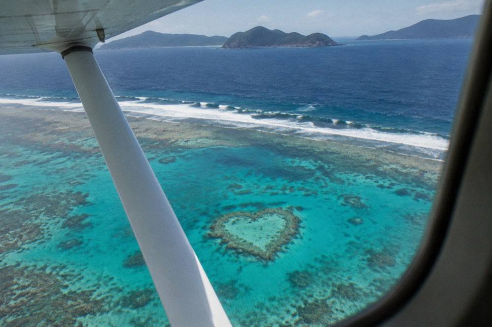 A light aircraft flying low over turquoise reef water near a heart shaped coral formation