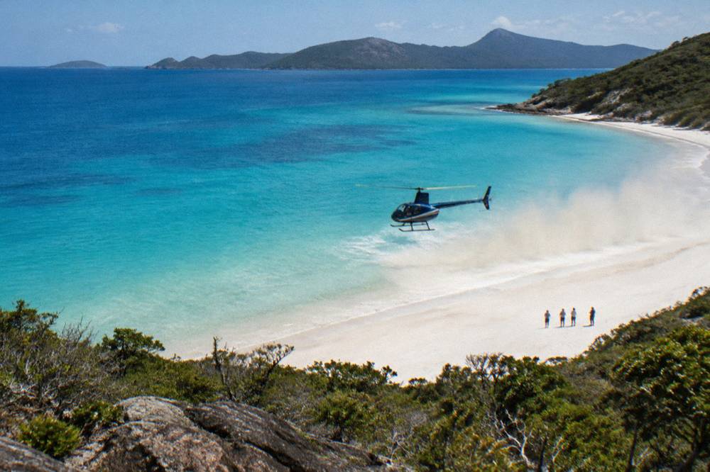 A helicopter hovering above white silica sand and turquoise water at Whitehaven Beach