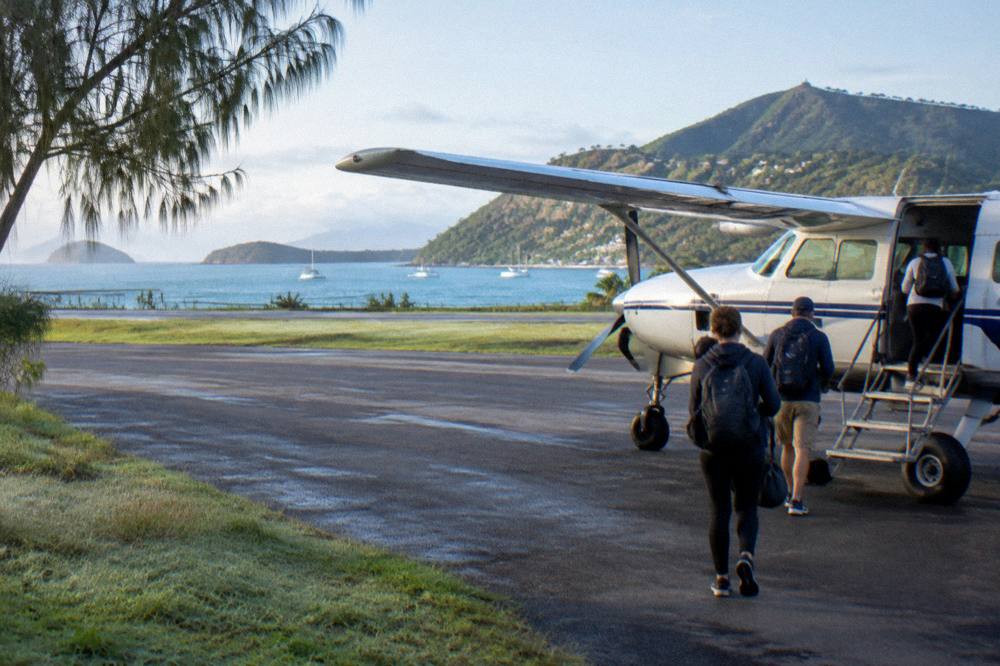 Passengers boarding a small high wing aircraft on a tropical airstrip near the water