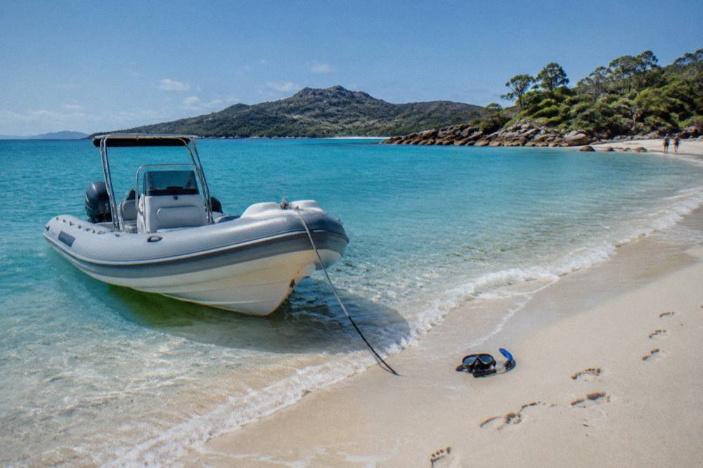 Rigid inflatable speedboat moored beside white sand and turquoise shallow water