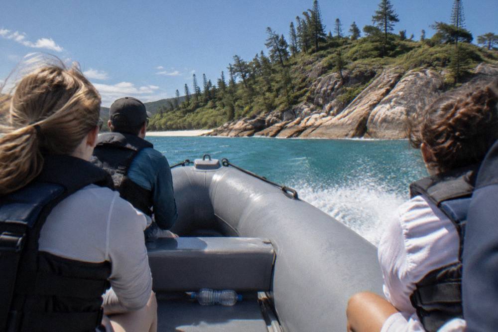 Passengers in life jackets seated along the side tubes of a moving inflatable boat