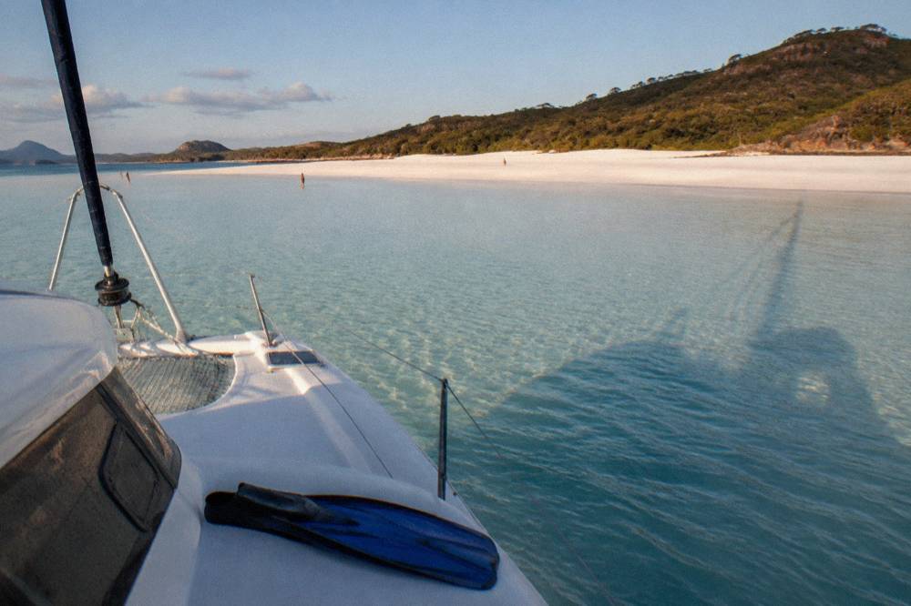 A sailing yacht moored near white silica sand and turquoise shallows