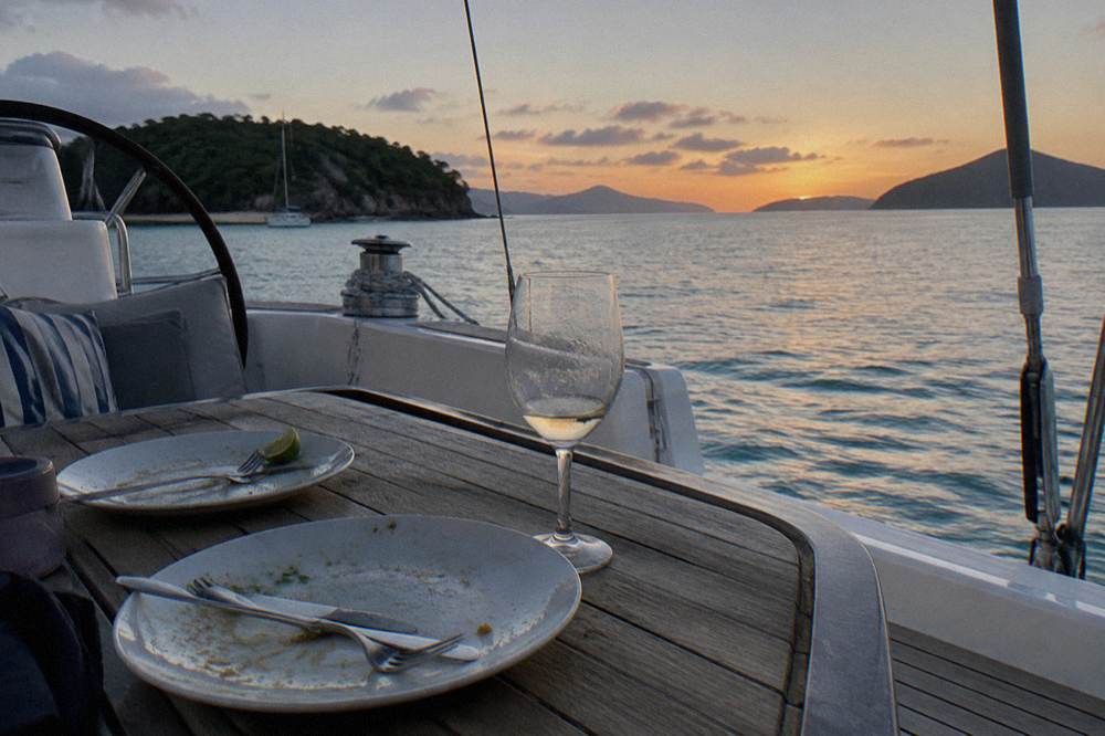 A yacht deck at anchor with calm evening water and island silhouettes