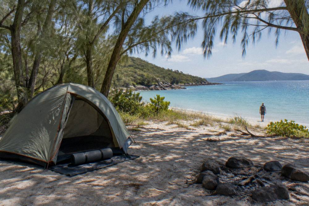 A tent set up behind a sandy beach on a wooded Whitsunday island