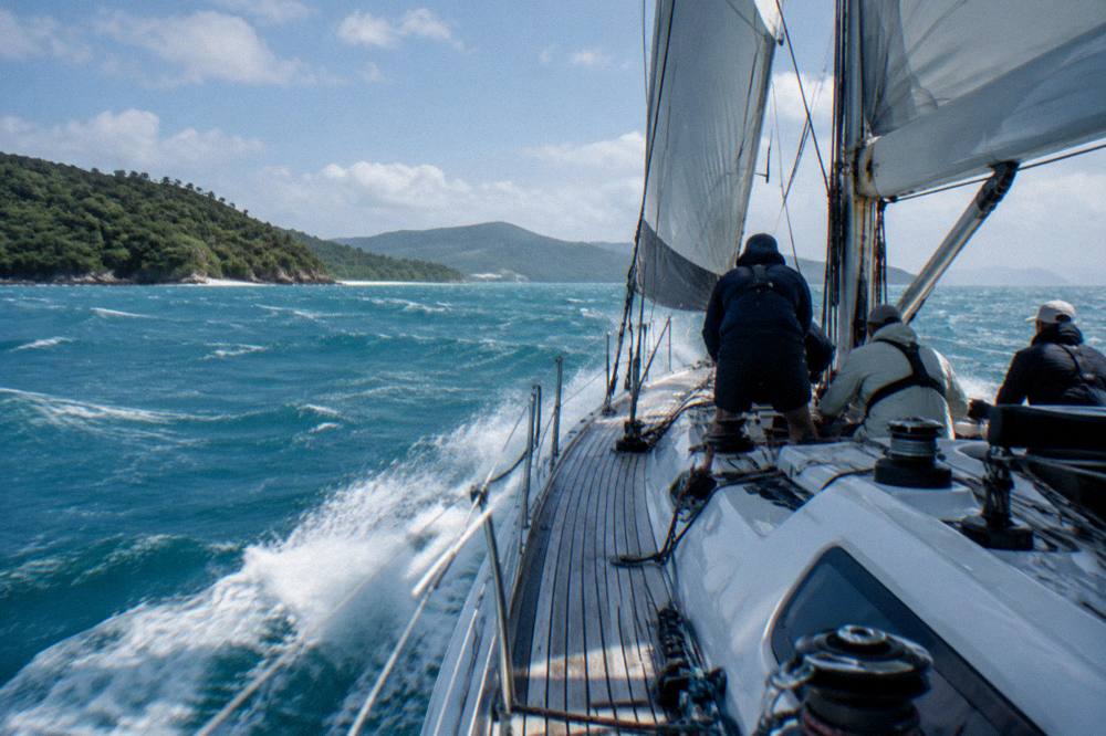 A maxi yacht under sail in open water between green islands