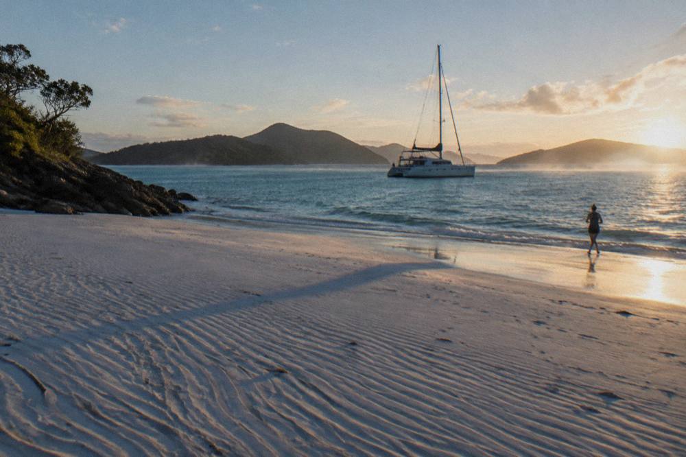 A high-speed touring catamaran moored beside a white silica beach with forested hills behind