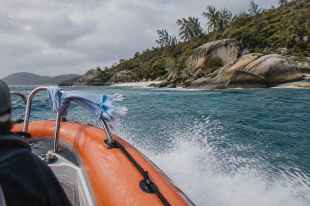 A small orange rigid-inflatable tour boat planing across open water between islands