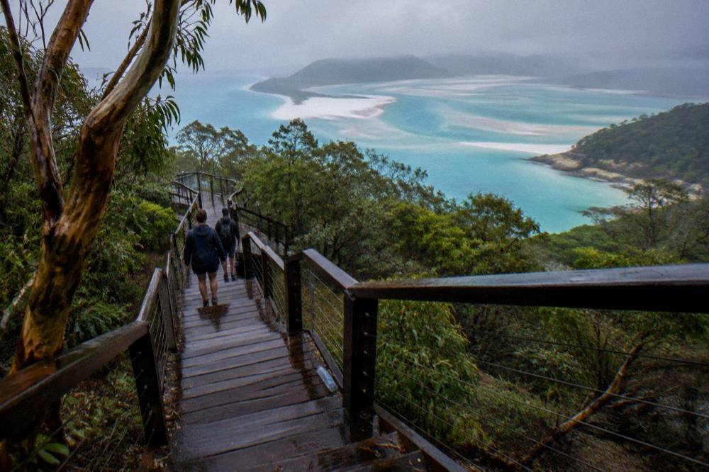 Tour passengers walking a timber boardwalk toward a lookout over a turquoise tidal inlet