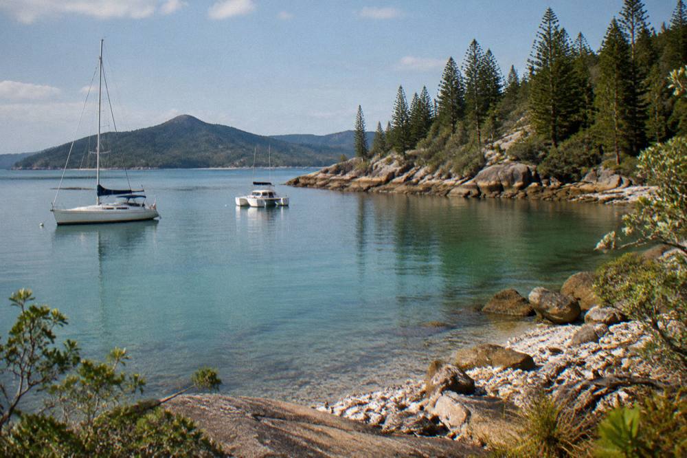 A white sailing yacht and a catamaran at anchor in a calm bay between green islands