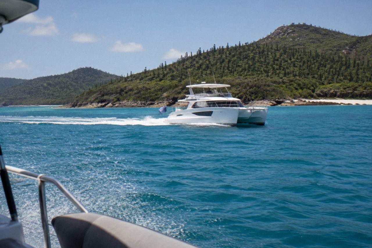 A multi-hull tour vessel cruising past green Whitsunday islands in calm blue water