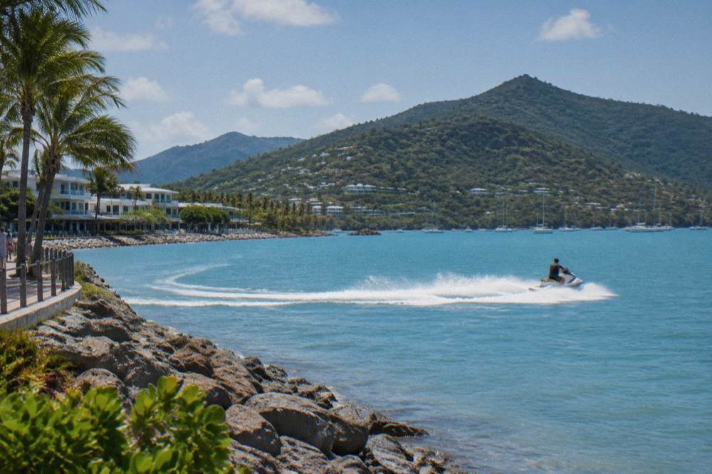 Jet ski cutting across calm blue water with forested hills behind