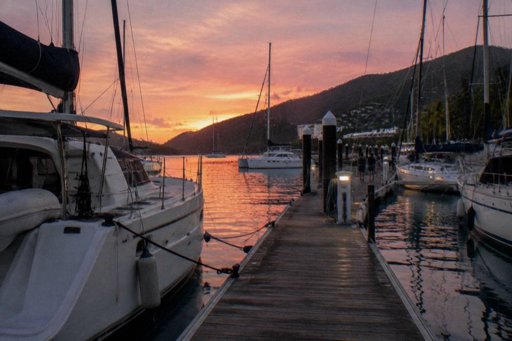Timber jetty at sunset with boats moored and pink sky over the water