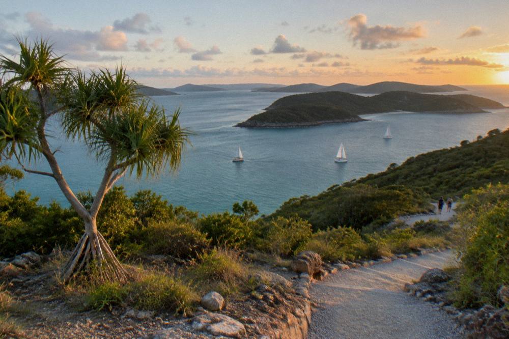 Sailing yachts crossing open water between green islands under scattered clouds