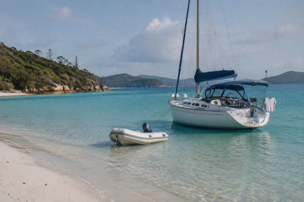 A sailing yacht anchored near a long white beach with clear shallow water