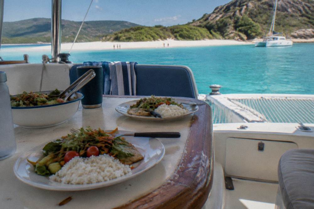 A shaded cockpit of a sailing catamaran with a plated lunch set on a table