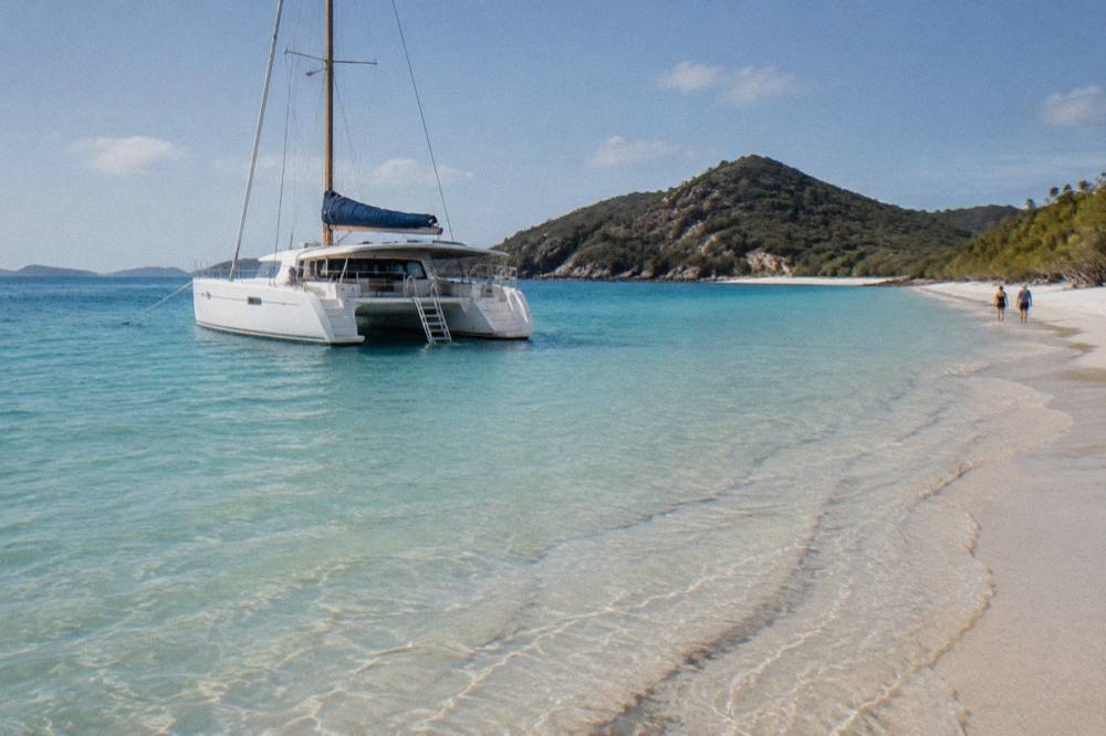 A white catamaran moored beside pale sand and clear shallow water