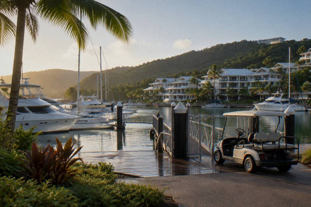 Resort buildings and palm trees above a calm marina with anchored yachts