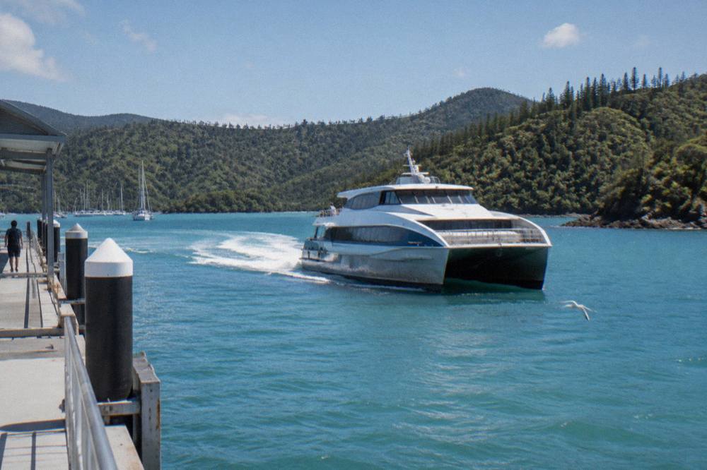 A fast catamaran ferry cruising past green island hillsides at midday