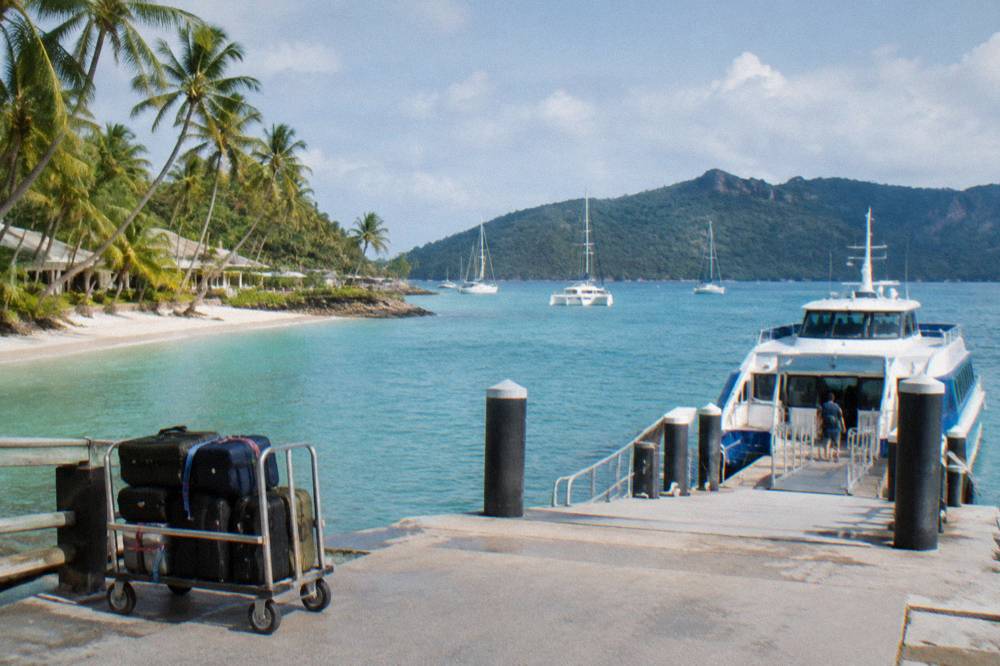 A ferry berthed at a island marina pontoon with anchored yachts behind