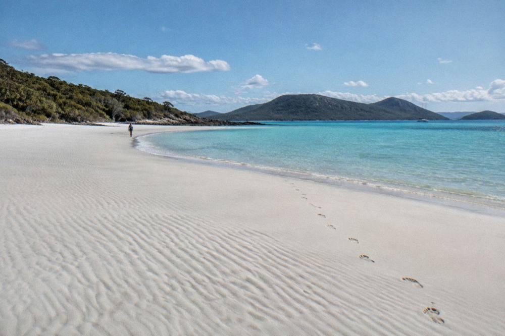 A long stretch of white silica sand curving toward turquoise shallow inlet water